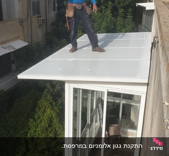 אדם עומד על גג לבן עם כלי עבודה ביד